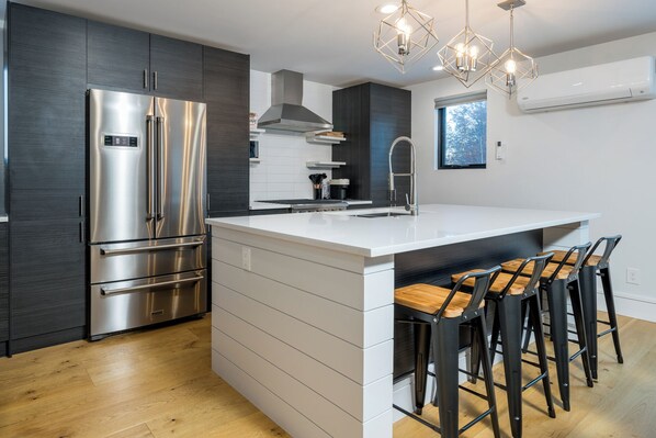 A modern kitchen with a stainless steel refrigerator, a central island with bar stools, and a window providing natural light.