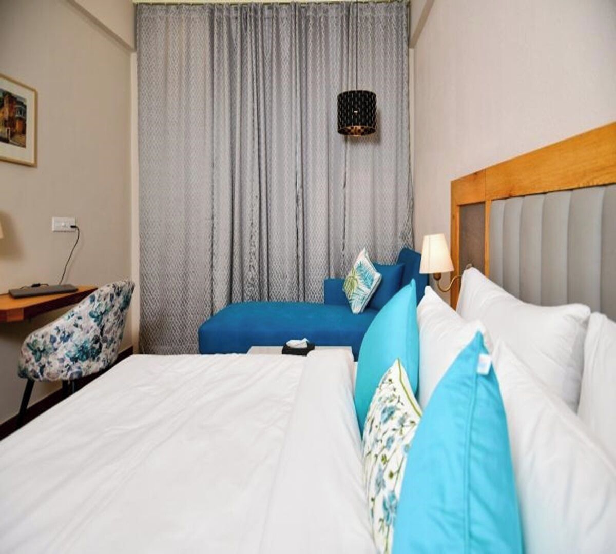 A hotel room with a large bed, a smaller sofa bed, a chair, a desk, and a window with curtains.