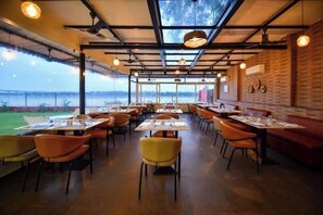 Een restaurant met een hoge plafond, zichtbare balken en uitzicht op de omgeving. Tafels en stoelen zijn er gezet voor het diner.