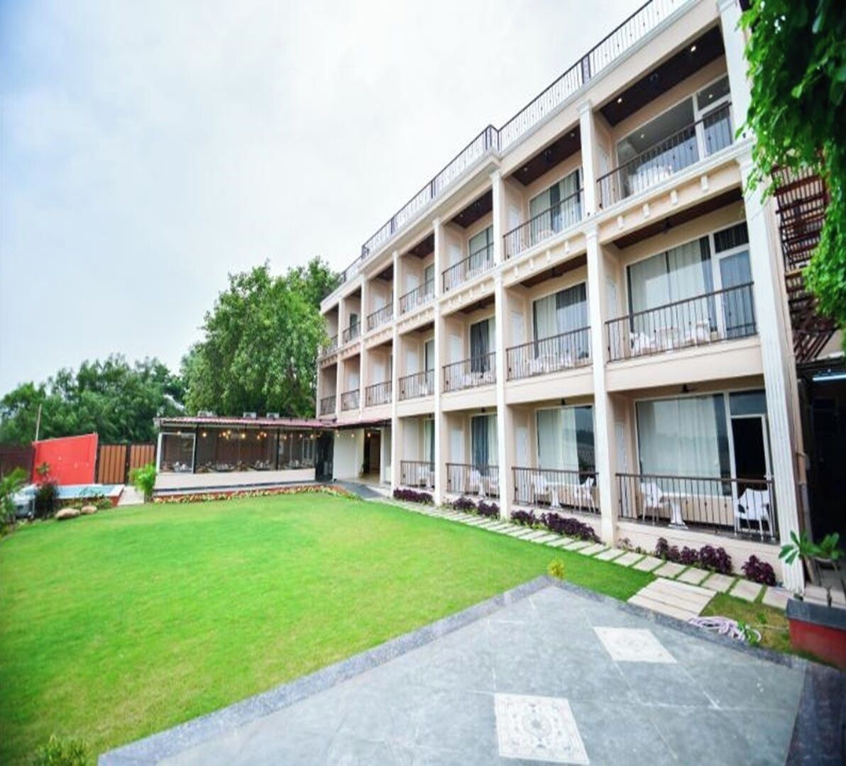 A multi-story hotel with balconies, a well-maintained lawn, and a small outdoor seating area.