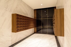 A modern hotel lobby with marble flooring, a wooden storage unit with numbered compartments, and a dark glass partition. - The Metropole Signature Residence by CR Concept (Ho Chi Minh City)