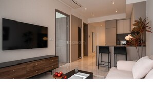 A modern living room with a flat-screen TV, a wooden cabinet, a coffee table with apples and a glass of water, and a sofa. - The Metropole Signature Residence by CR Concept (Ho Chi Minh City)