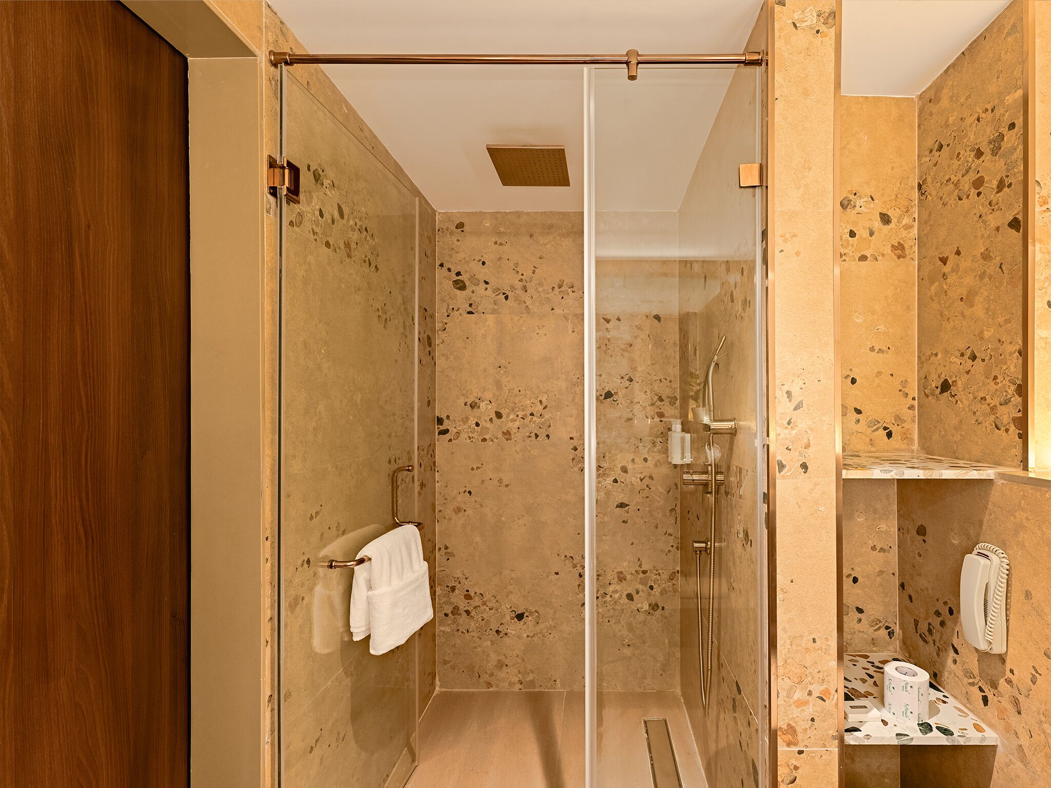 Un baño moderno con ducha de vidrio, puerta de madera y pared de mármol.