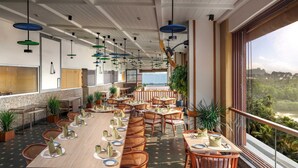 A spacious restaurant with multiple dining tables and chairs, large windows offering a view of the outdoors, and hanging pendant lights. - Gateway Goa, Palolem (Canacona)