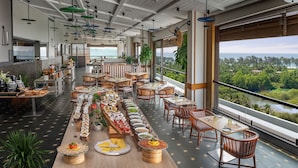 A spacious restaurant with long communal tables, a variety of dishes, and a scenic view of a river and greenery. - Gateway Goa, Palolem (Canacona)