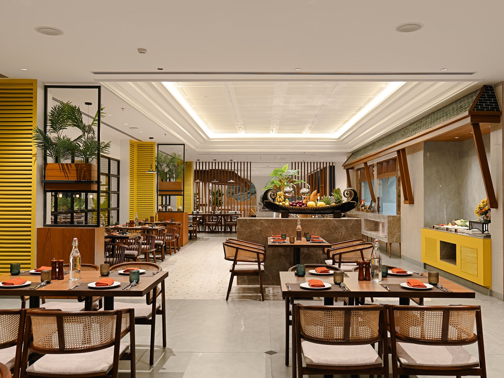 A spacious restaurant with high ceilings, natural light, and a central island with a fruit display.