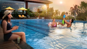 A pool area with lounge chairs and umbrellas, surrounded by a building with balconies. - Gateway Goa, Palolem (Canacona)