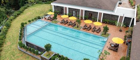 A large swimming pool with lounge chairs and umbrellas, surrounded by a landscaped garden and palm trees.