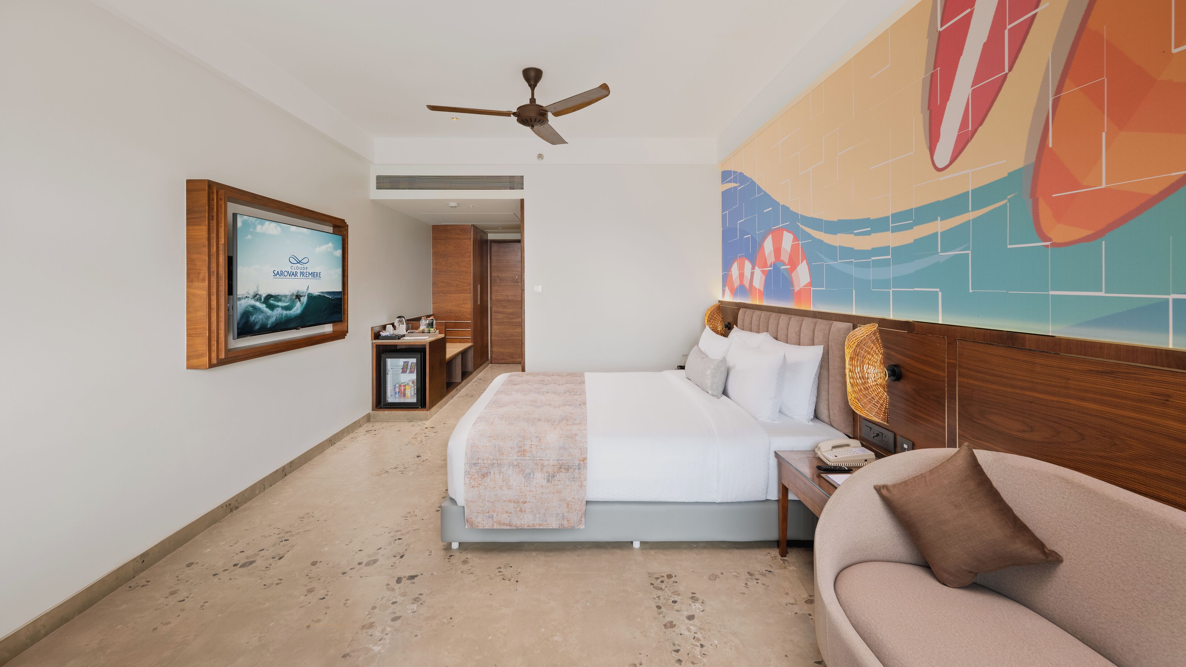 A hotel room with a bed, a sofa, a television, and a ceiling fan.