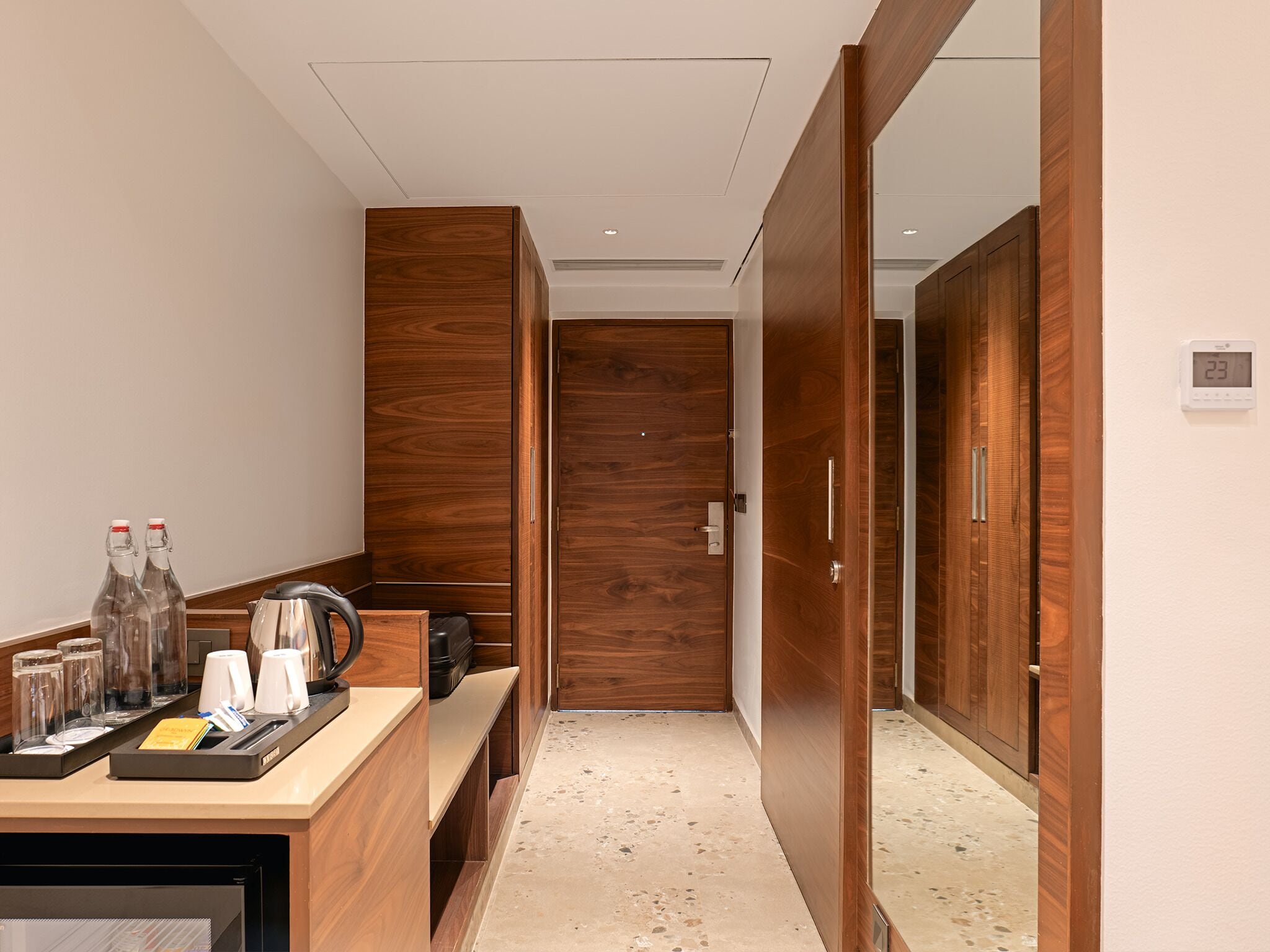 Een hotelkamer met een houten garderobe, een minibar en een koffiehoek.
