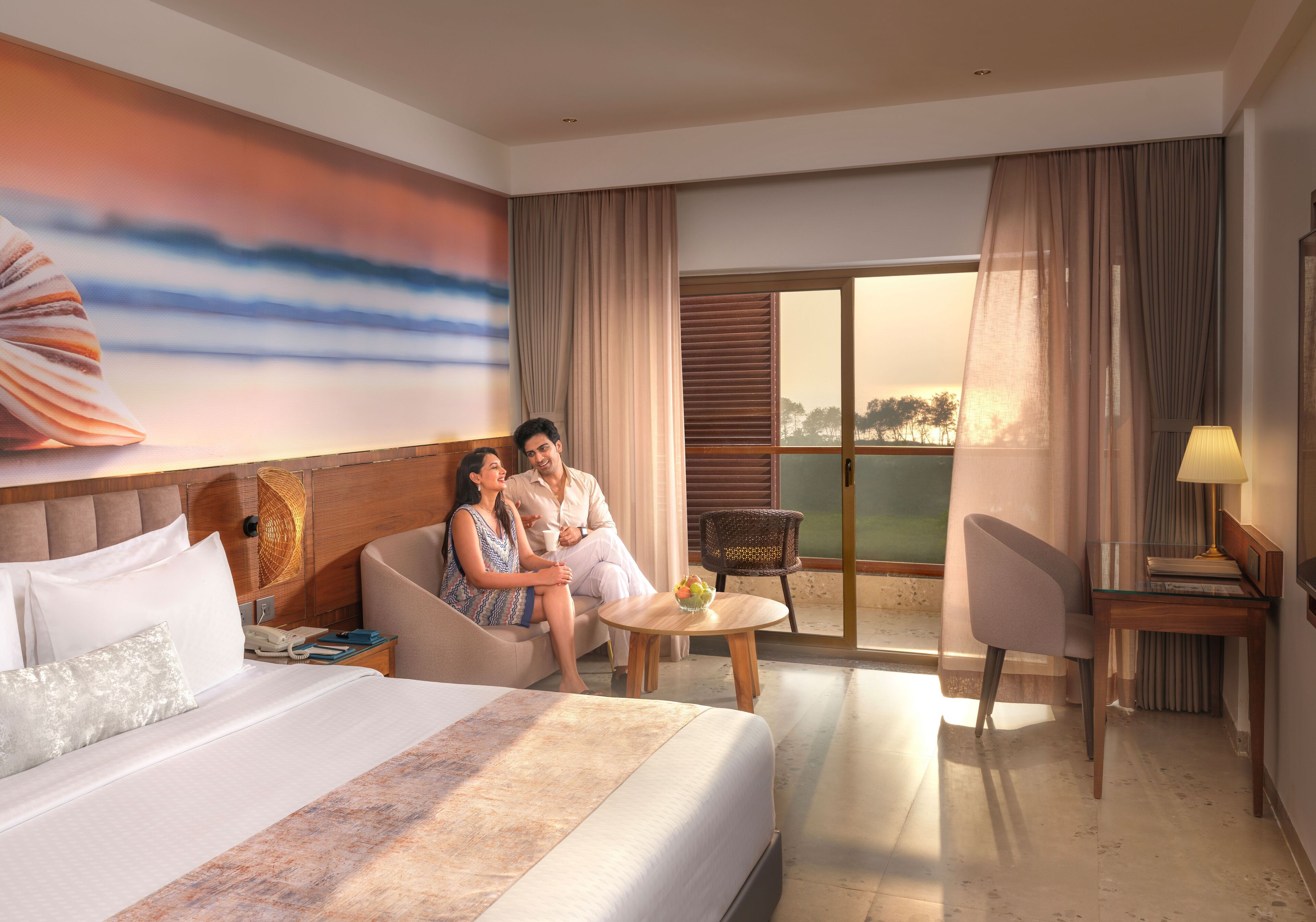 Habitación de hotel con una cama grande, un sofá, una mesa de comedor y vistas al exterior.