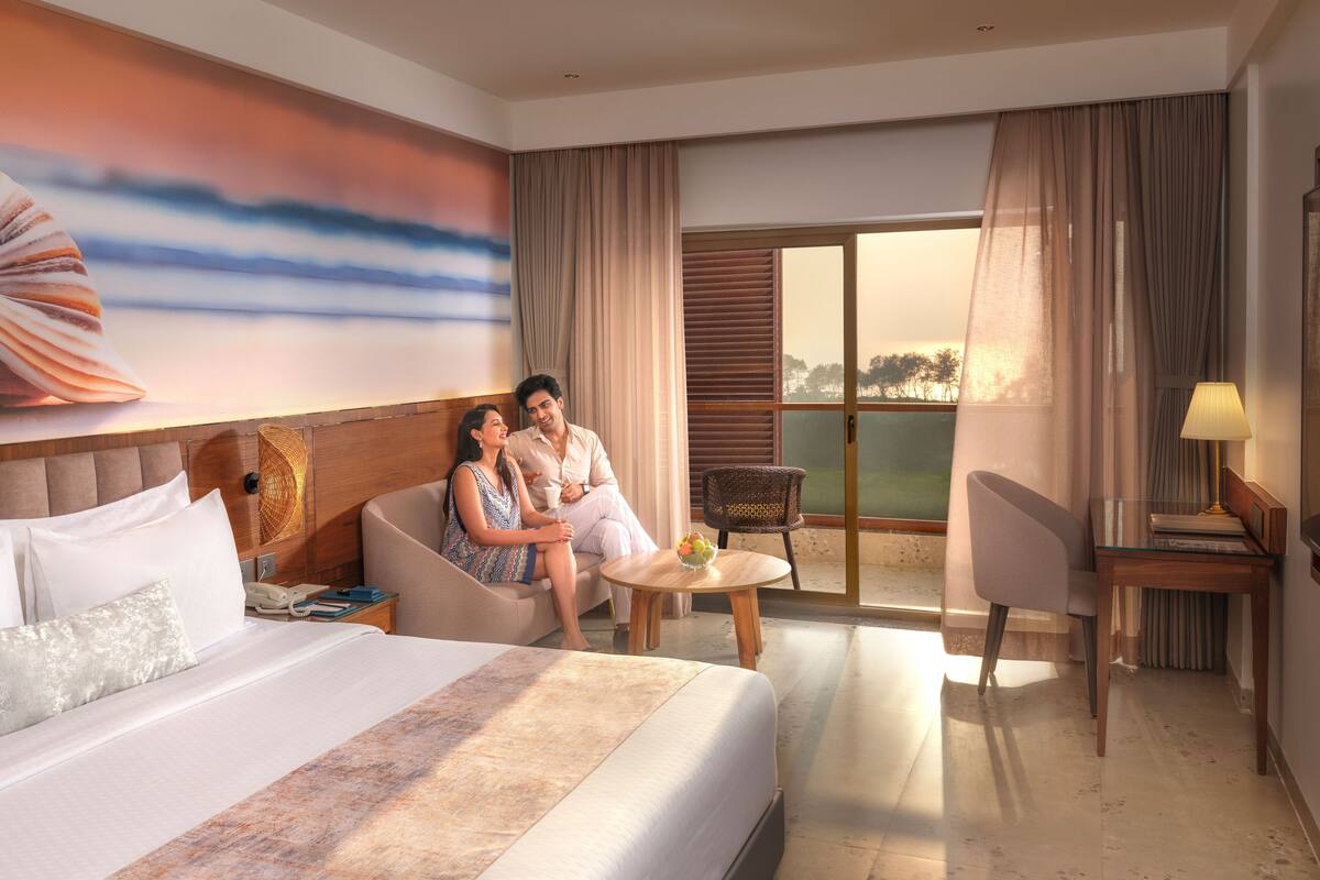 A hotel room with a large bed, a sofa, a dining table, and a view of the outdoors.