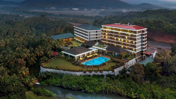 Un hotel grande con varios pisos, piscina y rodeado de vegetación exuberante y montañas.