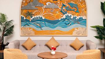 A living room with a sofa, two armchairs, a coffee table, and a large wall mural depicting a tropical scene with waves, a moon, and a dolphin.