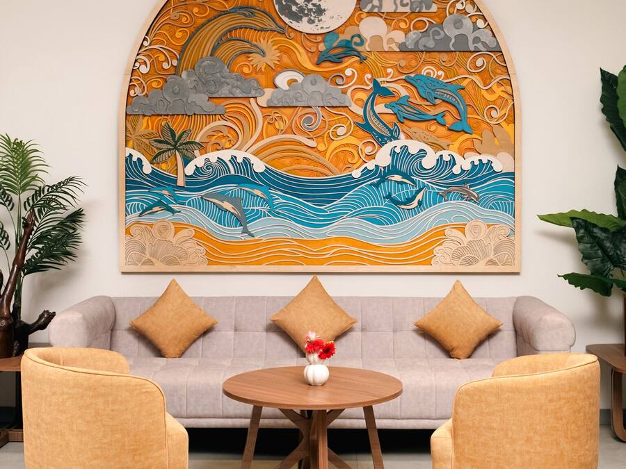 A living room with a sofa, two armchairs, a coffee table, and a large wall mural depicting a tropical scene with waves, a moon, and a dolphin.