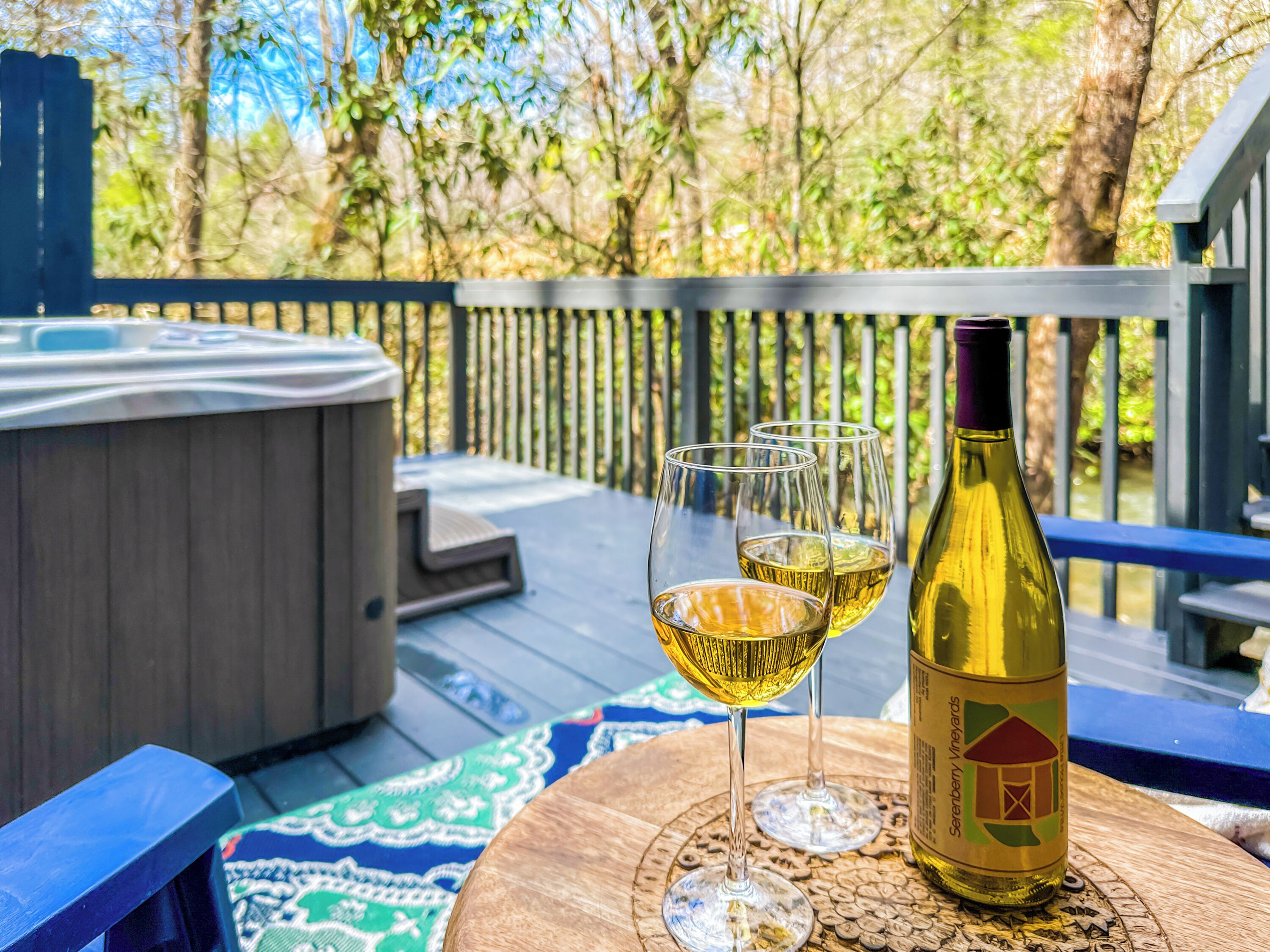 Un bain à remous sur une terrasse, avec une bouteille de vin et deux verres posés sur un dessous de verre.