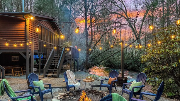A cozy outdoor seating area with Adirondack chairs, a fire pit, and string lights. - Creekside Adventure! 10 steps from the cascading and gentle Fightingtown Creek (Blue Ridge)