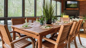 A wooden dining table set with chairs, surrounded by large windows offering a view of trees. - Creekside Adventure! 10 steps from the cascading and gentle Fightingtown Creek (Blue Ridge)