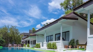 A swimming pool with a clear blue water surface, surrounded by a white building with large windows and a covered patio area. - The BRC Ao-nang HOTEL (Krabi)