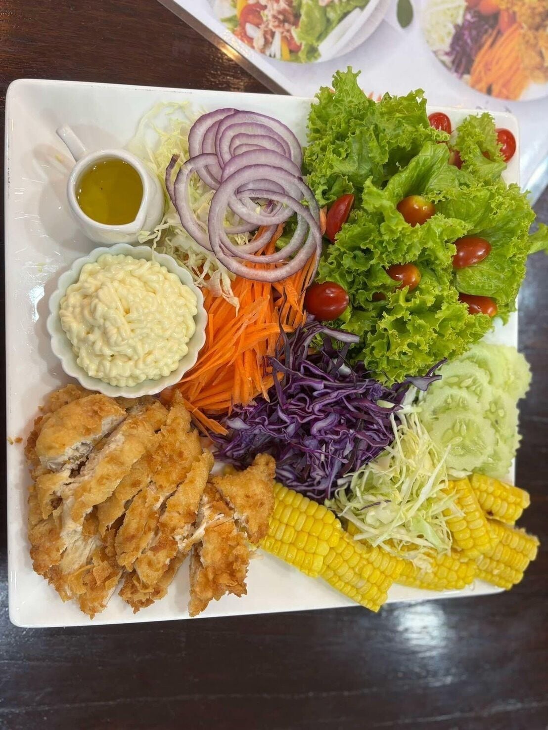 A plate with various vegetables, a small bowl of sauce, and a piece of fried chicken.
