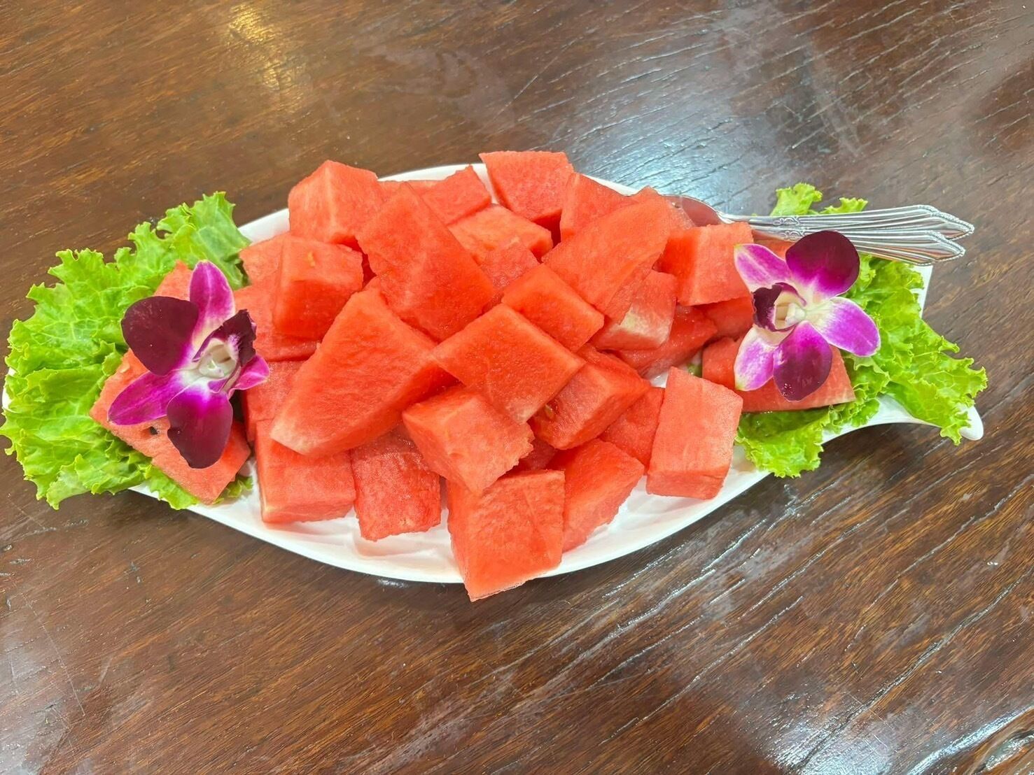 A plate of cubed watermelon with purple orchids on a wooden table.
