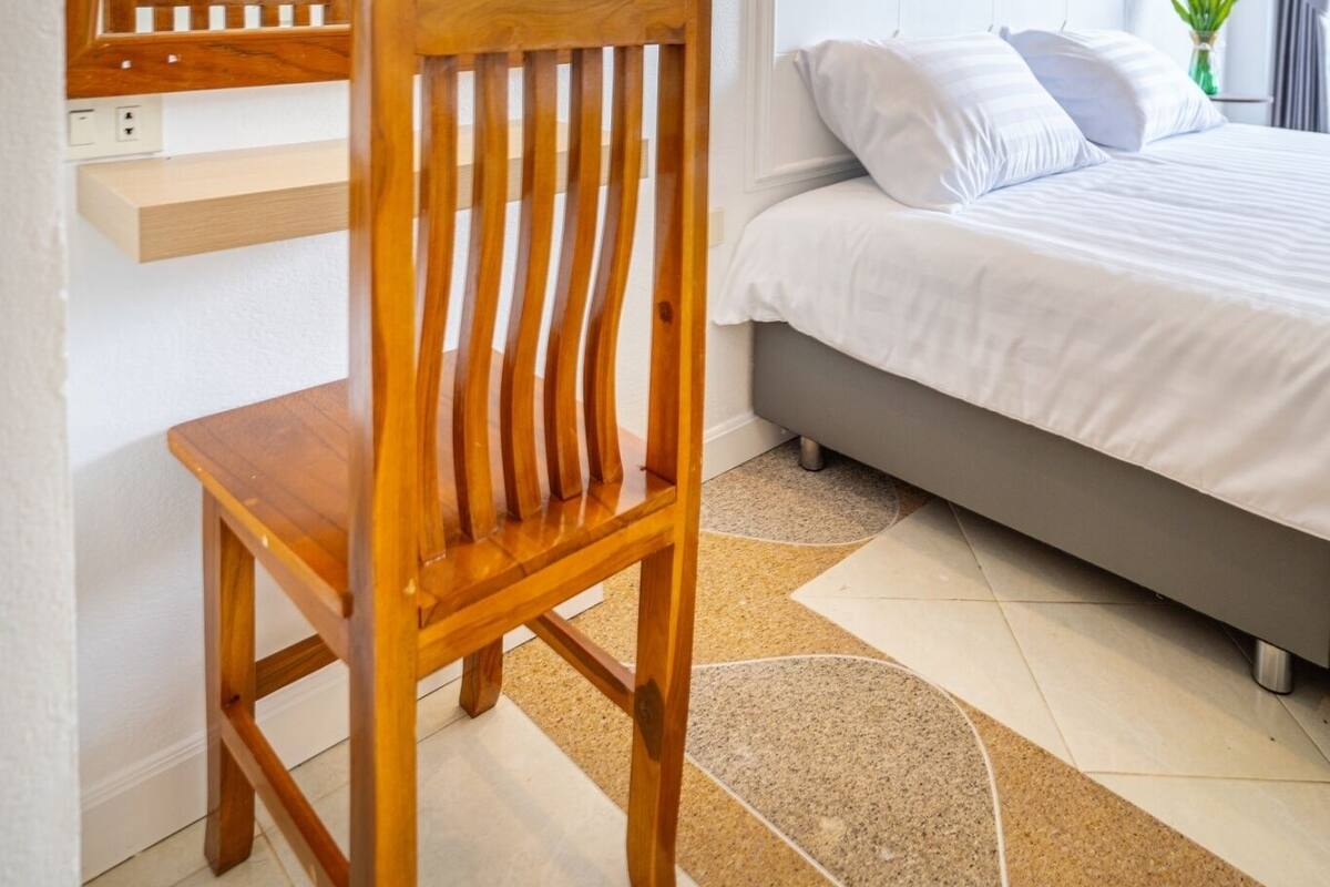 Ein Schlafzimmer mit Holzstuhl, einem Bett mit weißer Bettwäsche, einem großen Spiegel und einem Bild an der Wand.