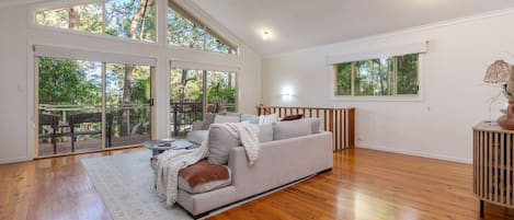 Un salon spacieux avec un grand canapé, un plancher en bois et de grandes fenêtres donnant sur la verdure.
