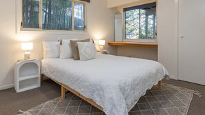 A bedroom with a bed, bedside tables, a nightstand, a mirror, and a window with a view of trees.