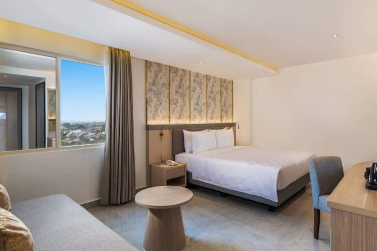 Een hotelkamer met een groot bed, een bureau, een stoel, een klein rond tafeltje en uitzicht op de stad.