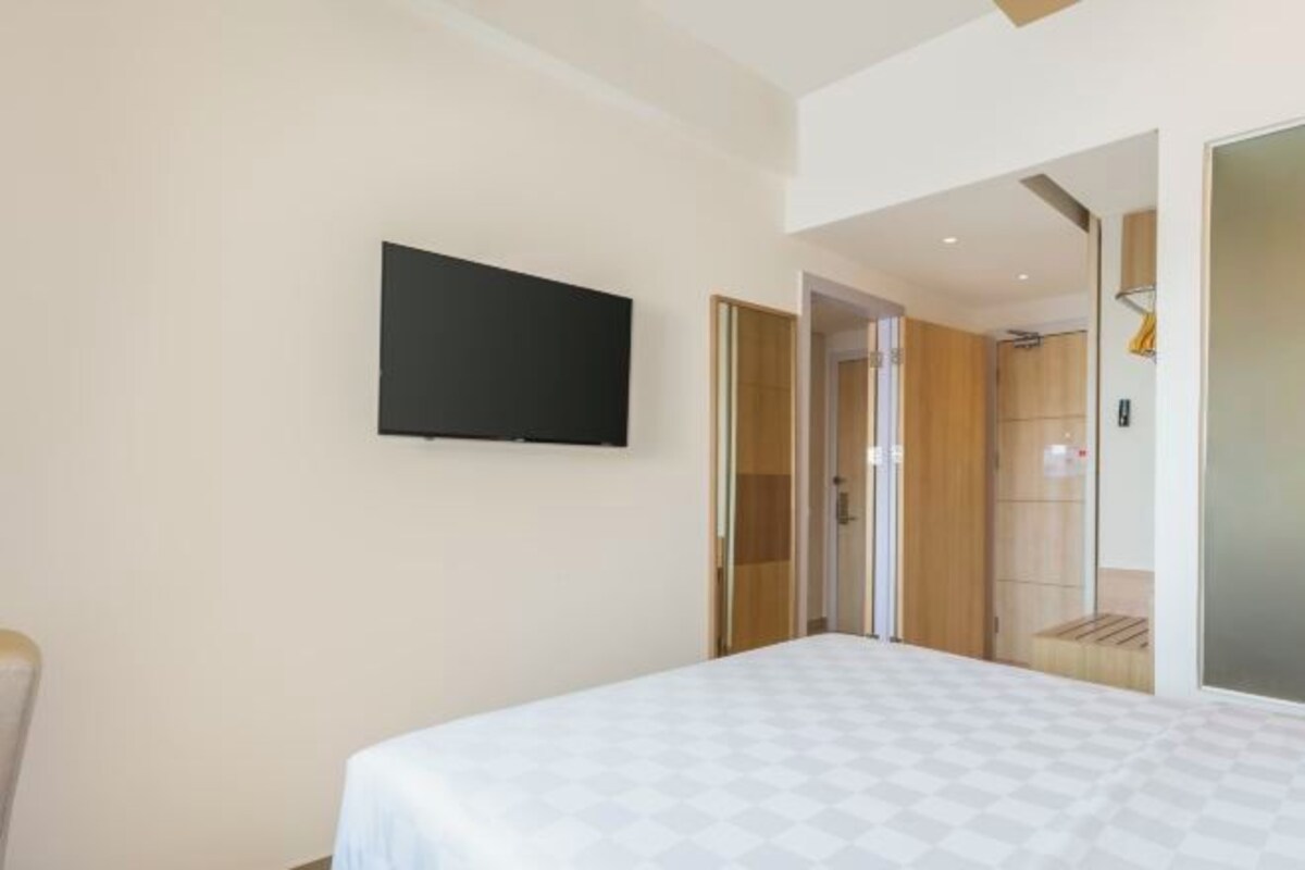 A modern hotel room with a large bed, a flat-screen TV mounted on the wall, and a sliding door leading to a shower area.