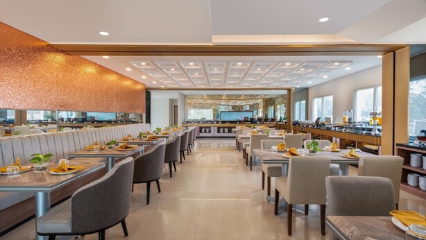 Een modern restaurant met een lange toonbank, meerdere eettafels en een hoge plafond met inbouwverlichting.