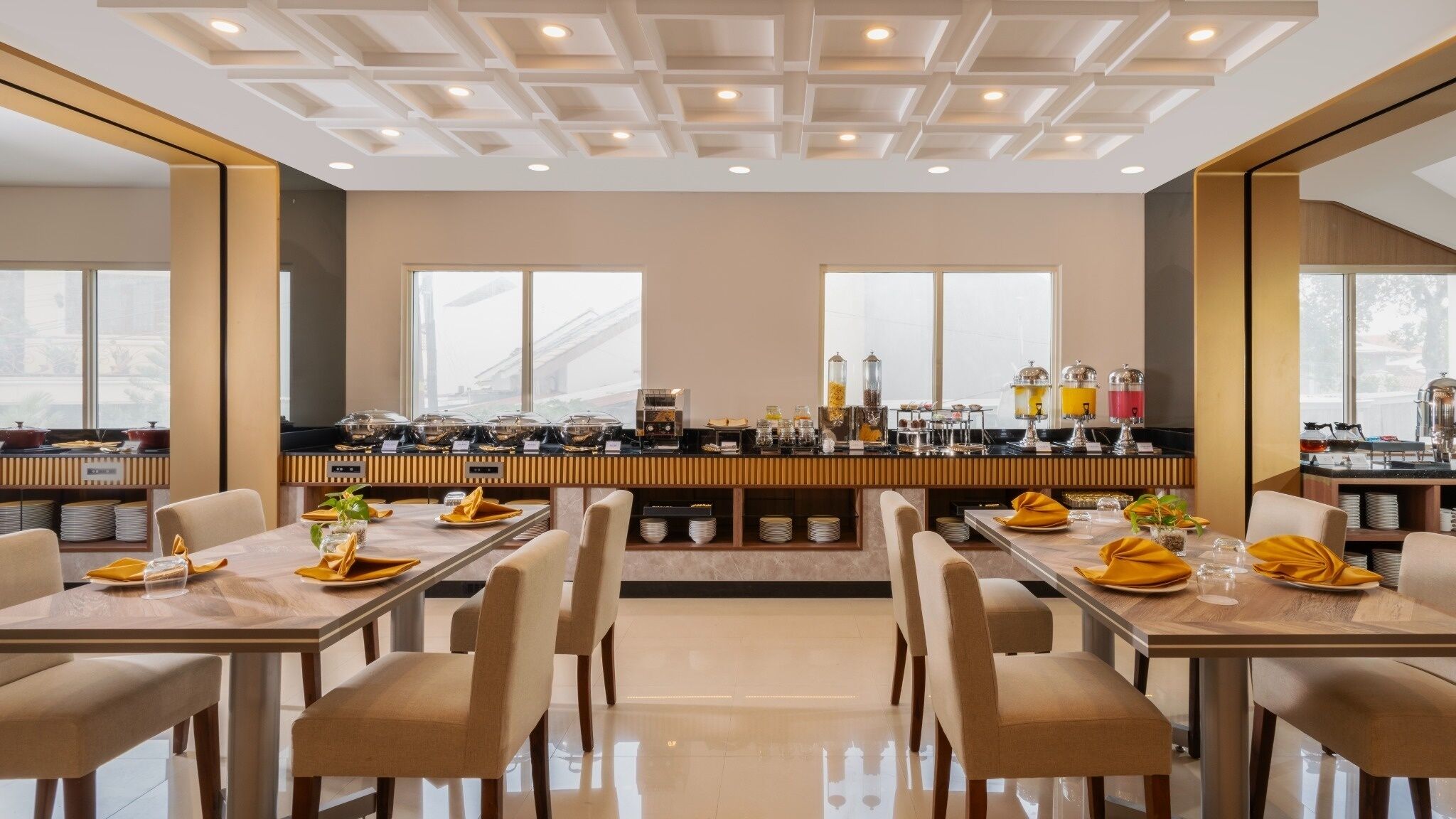 A modern dining area with a long counter, multiple seating arrangements, and a view of the city through large windows.