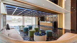 Een moderne lobby met een receptiebalie, een zithoek en een glazen plafond.
