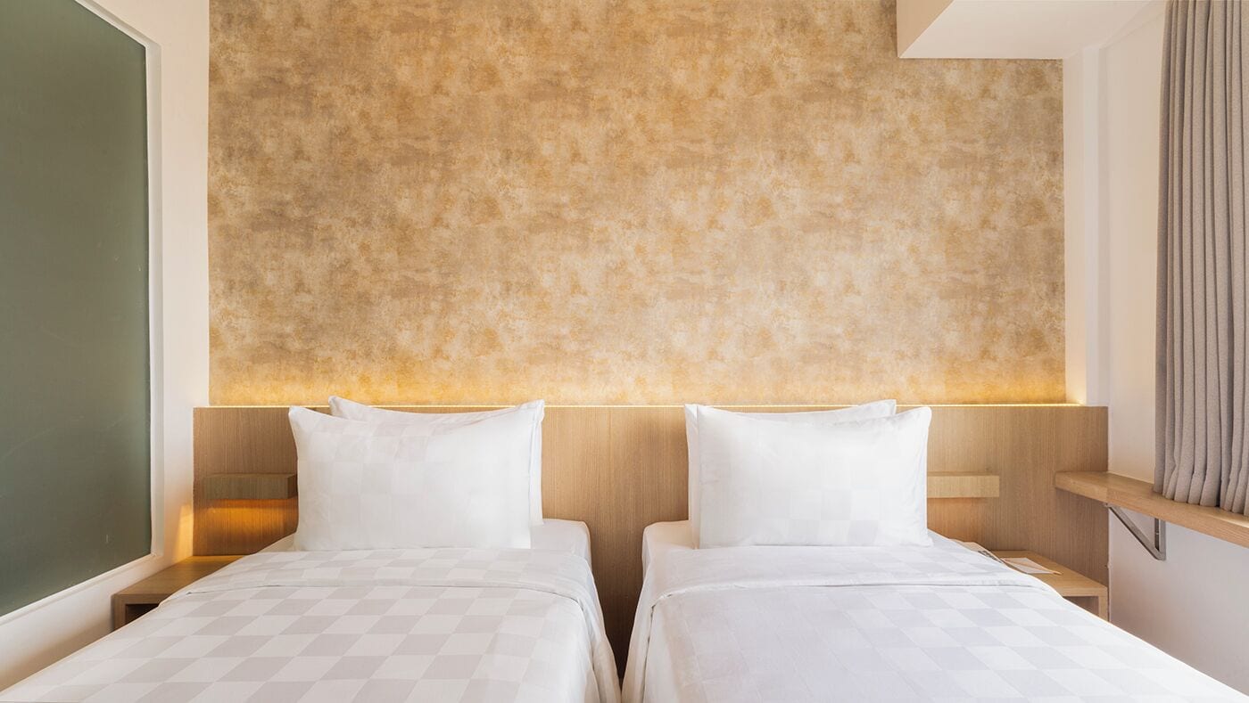 A hotel room with two beds, a textured wall, and a wooden headboard.