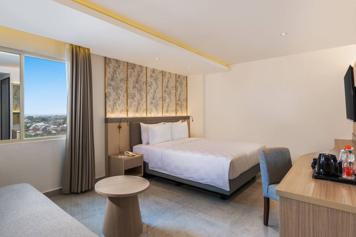 Ein Hotelzimmer mit Bett, Schreibtisch, Stuhl, rundem Tisch und Blick auf die Stadt.