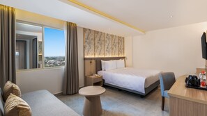 Une chambre d’hôtel avec un lit, un bureau, une chaise, une table ronde et une vue sur la ville.