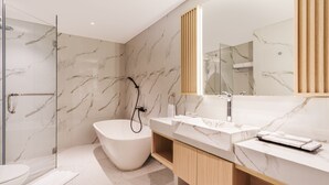 Een moderne badkamer met een vrijstaand bad, een glazen douchecabine en een grote spiegel met een houten paneel.
