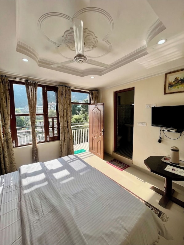 Quarto com cama, televisão, escrivaninha e janela com cortinas.