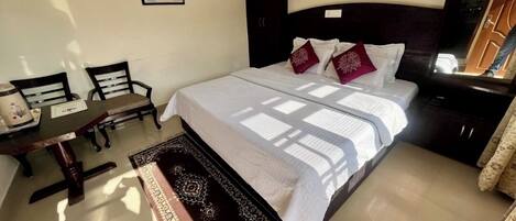 A bedroom with a bed, a desk, two chairs, a dark-colored wardrobe, and a patterned rug.