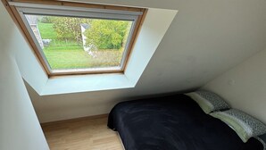 Une petite pièce avec un toit en pente et une lucarne, un lit et un radiateur.