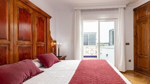 Habitación de hotel con una cama grande, un armario de madera y un balcón con vistas.