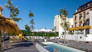 Zona de piscina con una fuente, palmeras y mobiliario de exterior.