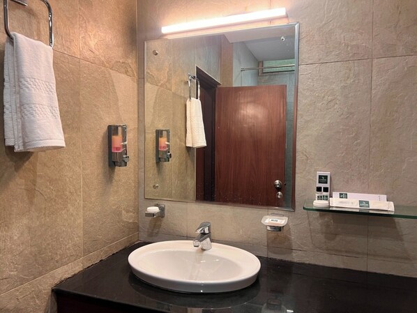 A bathroom with a round sink, a mirror, a towel rack, and a soap dispenser. - Hotel Park Royale Inn (Dehradun)