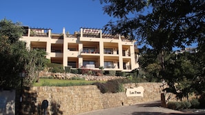 A multi-story building with balconies, a stone wall, and a sign reading "Los Pinos." - Garden Apt In Los Pinos, Los Arqueros Golf (Benahavis)