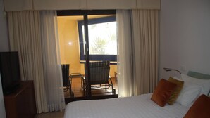 A hotel room with a bed, a TV, a balcony with a chair, and curtains. - Garden Apt In Los Pinos, Los Arqueros Golf (Benahavis)