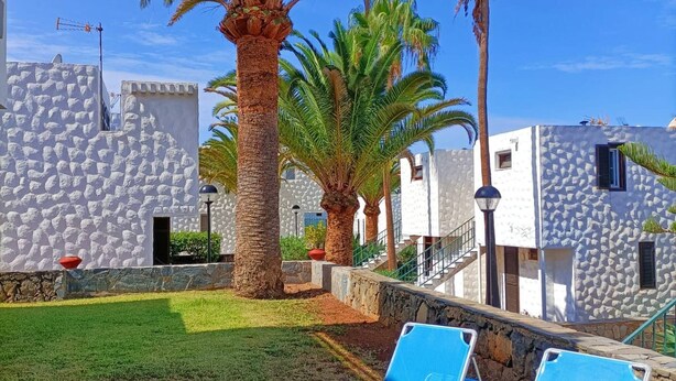 A resort with stone buildings, palm trees, and two blue lounge chairs on a grassy lawn. - Playa D Las Américas-casa Rucaba (Adeje)
