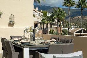 A dining table set for four with a view of palm trees and buildings in the background. - El Casar Townhouse Benahavis (Benahavis)