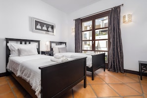A hotel room with two beds, a large window with curtains, a framed picture on the wall, and a small table with a lamp. - El Casar Townhouse Benahavis (Benahavis)