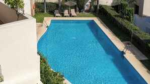 A rectangular swimming pool with clear blue water, surrounded by a well-maintained lawn and palm trees. - El Casar Townhouse Benahavis (Benahavis)