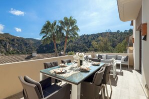 A dining area with a table set for four, overlooking a mountainous landscape with palm trees.
